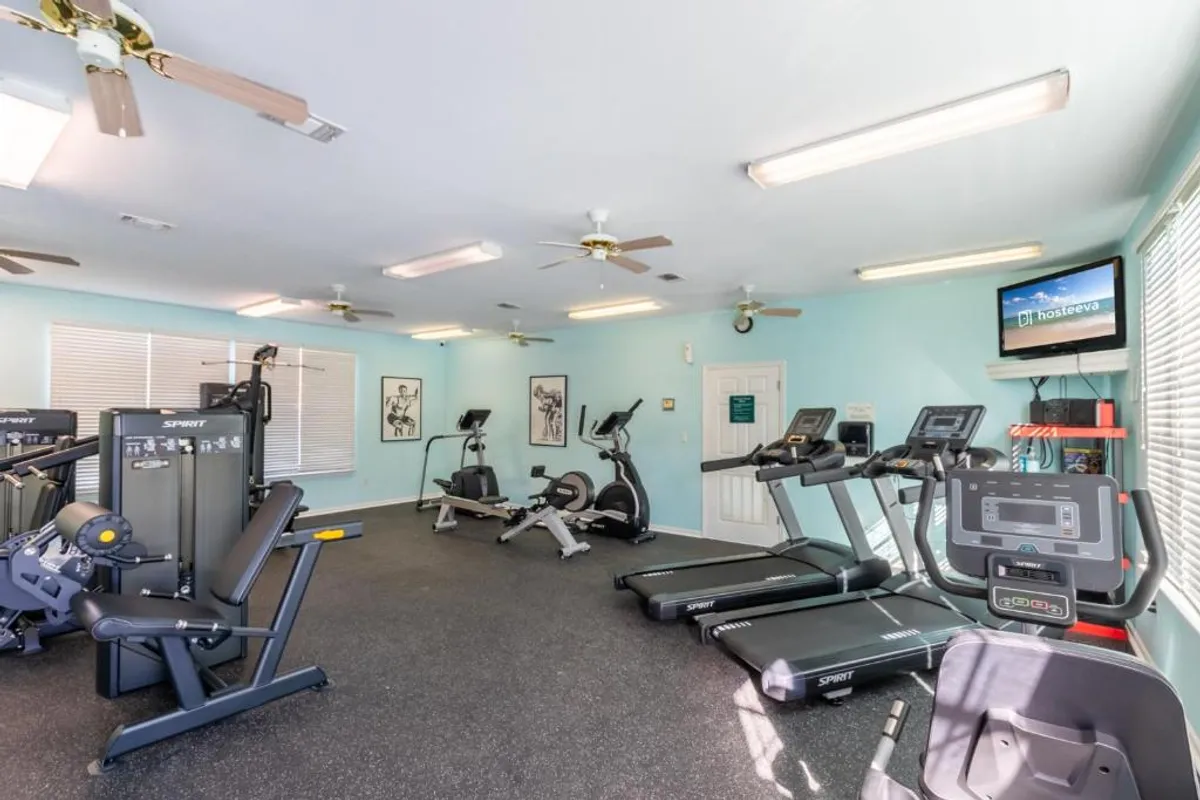An interior view of a modern fitness center equipped with treadmills, exercise bikes, weight machines, and a television screen. The space is bright and organized, offering an energetic environment for workouts and group fitness.