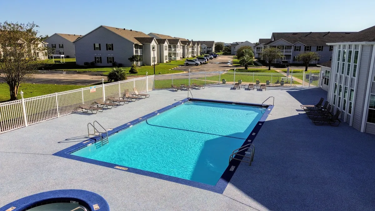 A vibrant outdoor scene featuring a sparkling swimming pool and inviting hot tub surrounded by lounge chairs and lush green lawns, with apartment buildings in the background. The area exudes a resort-inspired atmosphere, ideal for relaxation and social gatherings.
