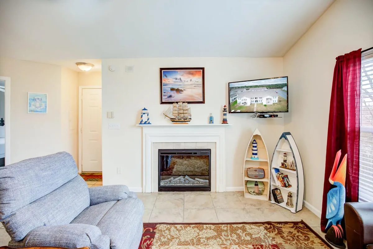 The hero image showcases a cozy living area featuring a welcoming fireplace with nautical decor, a mounted TV displaying an aerial view, a plush blue armchair, and unique boat-shaped bookshelves. The setup invites relaxation, family gatherings, and moments of conversation, all within a warm and inviting atmosphere.