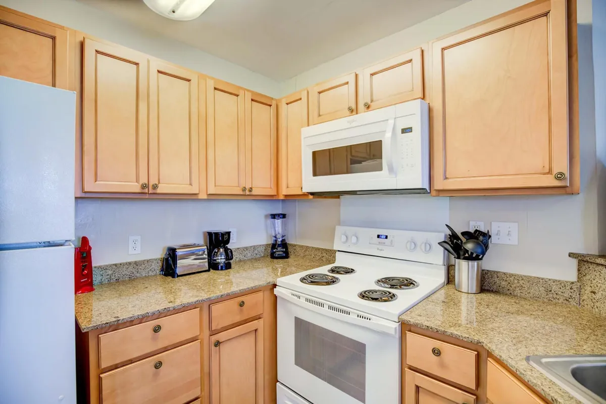 A practical kitchen view showing a white electric stove with oven, microwave above, wooden cabinetry, and granite countertops. The space is arranged for convenient meal prep and socializing while cooking.