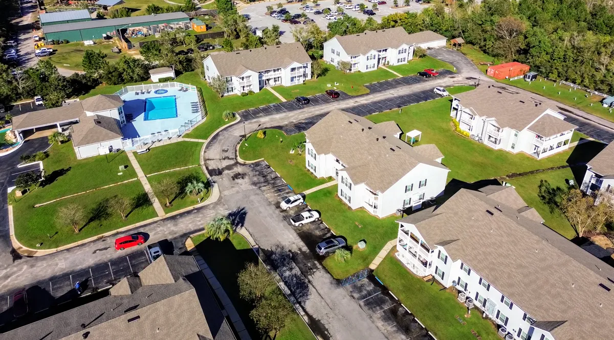 This exterior shot captures the community pool and hot tub area, surrounded by lounge chairs and set against a backdrop of 2-story condominium buildings, with parking areas and green lawns connecting the amenities. The image conveys a sense of relaxation and community, emphasizing the recreational spaces available to guests.